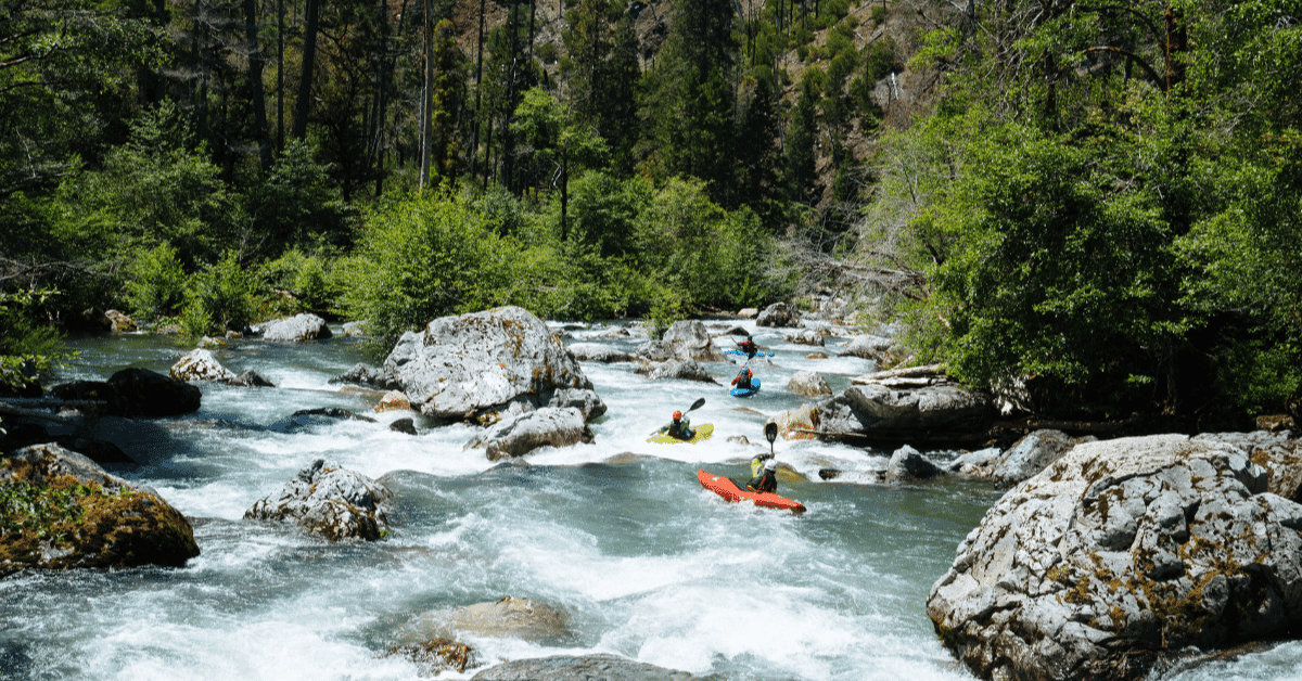 Whitewater kayakers in colorful boats paddle in a line through a rock garden of rapids on Indigo Creek, a tributary of the Rogue River