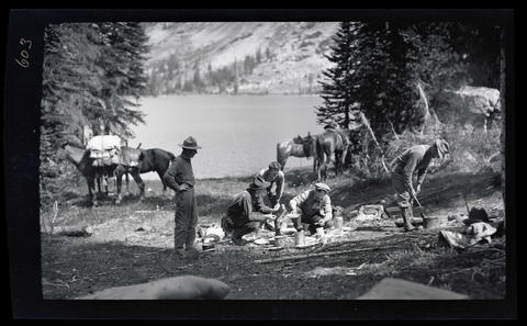 Dallas Lore Sharp (kneeling with pan and wearing a cap) and four unidentified men preparing a meal in their campsite in the Wallowa Mountains. Oregon Historical Society