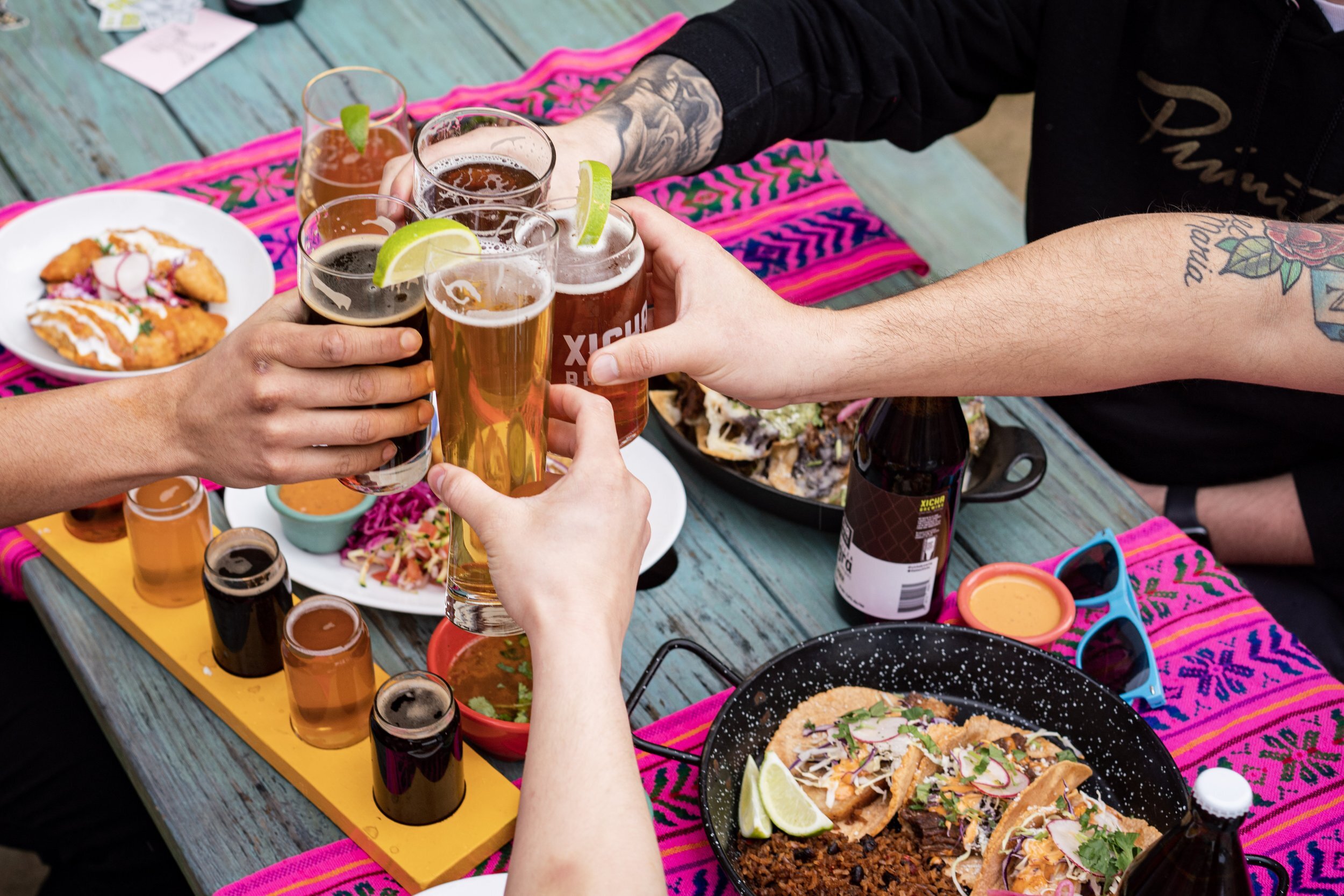 cheers! 4 friends clink glasses at the dinner table with delicious food, and brightly colored pink table settings